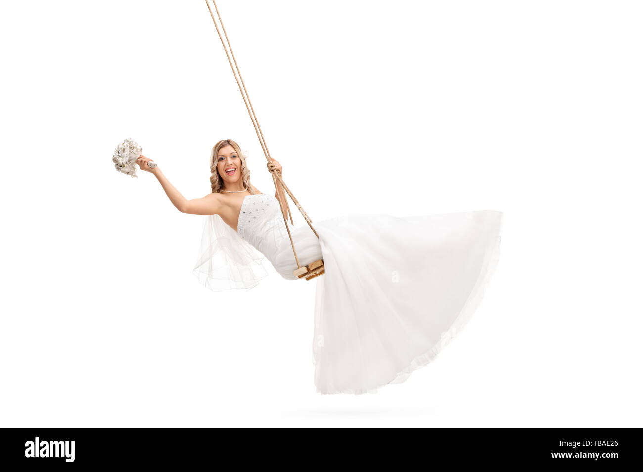 Carefree young bride swinging on a wooden swing and holding a wedding flower isolated on white background Stock Photo