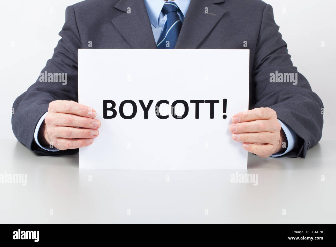 Man in suit sitting behind an office table and holds a white sheet with text Boycott in his hands. Stock Photo