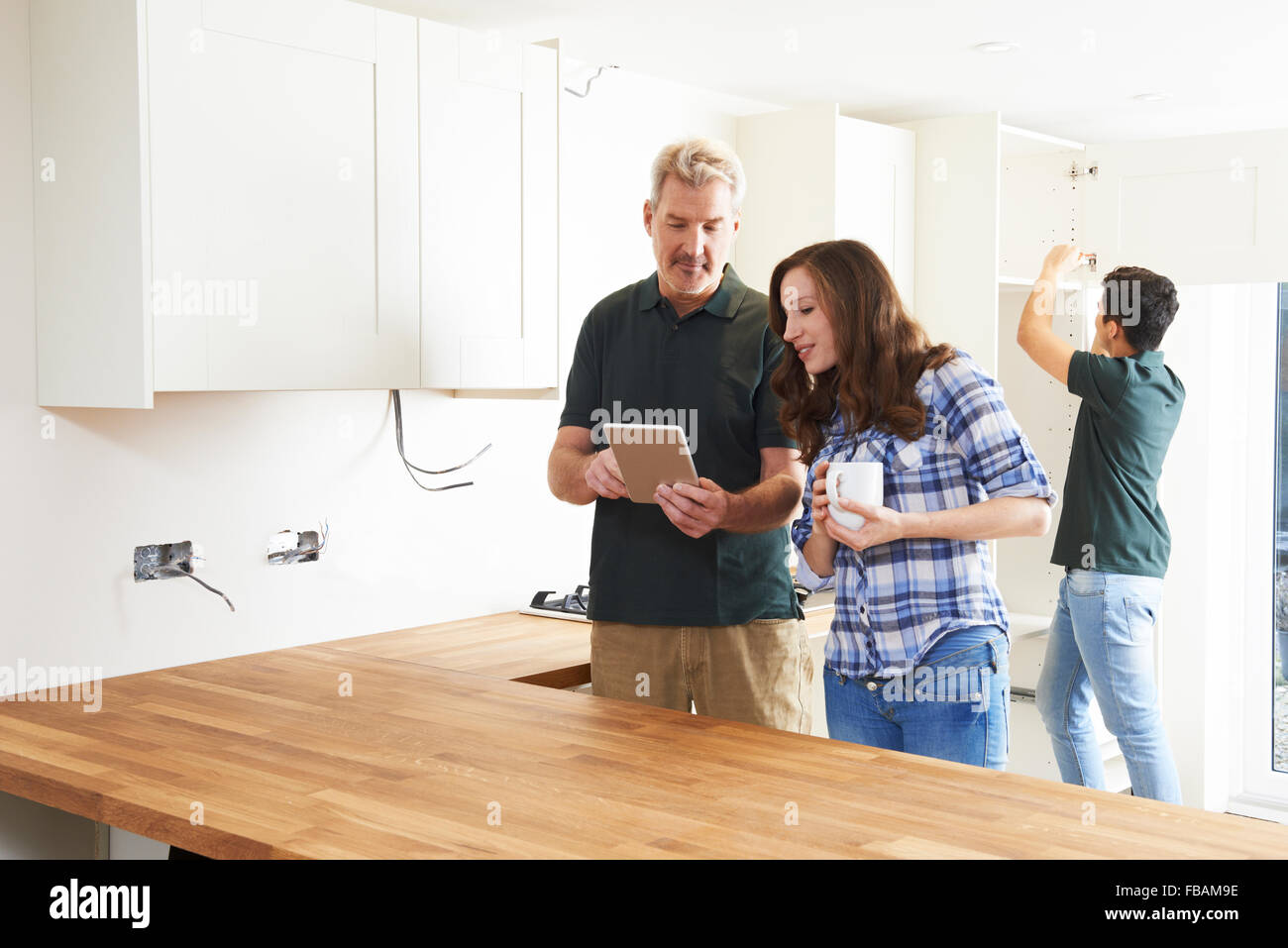 Woman With Carpenter Looking At Plans For Kitchen On Digital Tablet Stock Photo