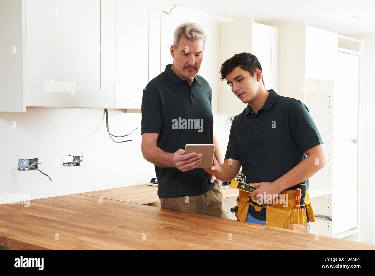 Carpenter And Apprentice With Digital Tablet Fitting Luxury Kitchen Stock Photo
