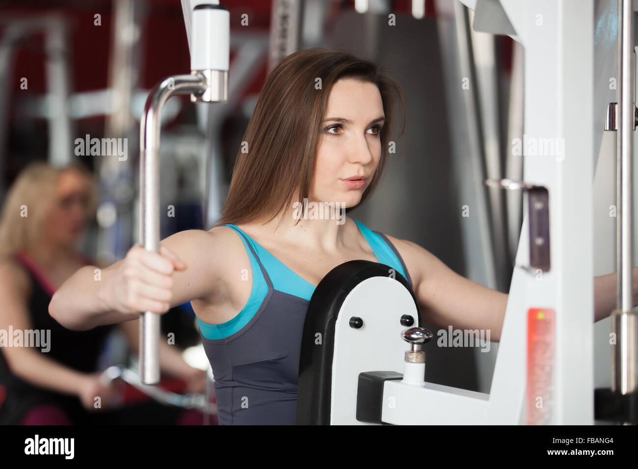 Girl in sportswear exhales while doing exercises for arms and shoulders on training apparatus in fitness center Stock Photo