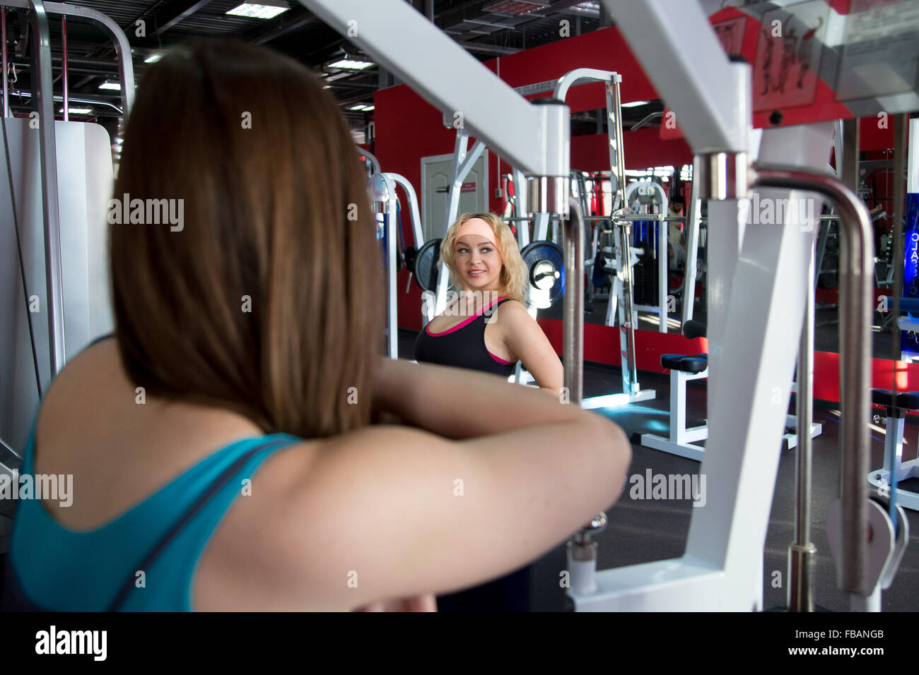 Two female bodybuilders in sportswear, one girl is exercising and another is watching her while resting Stock Photo