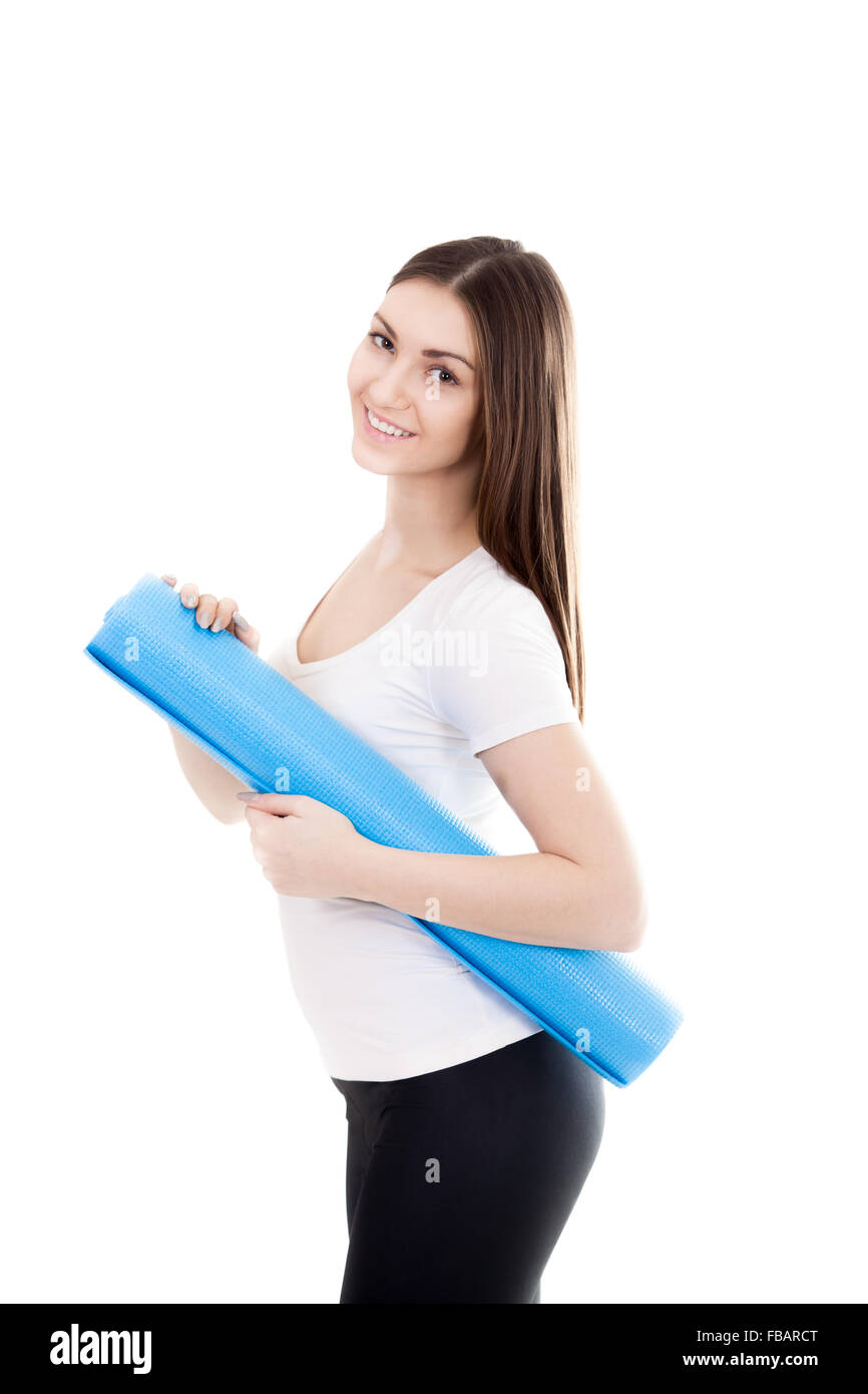Happy sporty beautiful yogi girl holding folded blue yoga mat, ready for fitness exercises. Healthy life, keep fit concepts. Iso Stock Photo