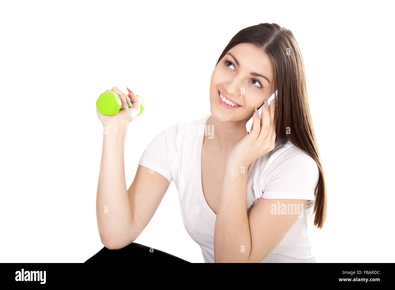 Young smiling teenage girl making call with smartphone, talking on the cellphone and lifting dumbbell weights, doing fitness exe Stock Photo