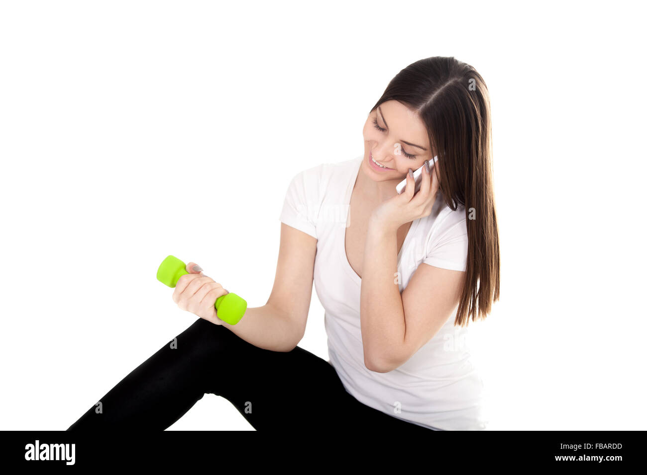 Young smiling teenage girl making call with smartphone, talking on the mobile phone and lifting dumbbell weights, doing biceps c Stock Photo