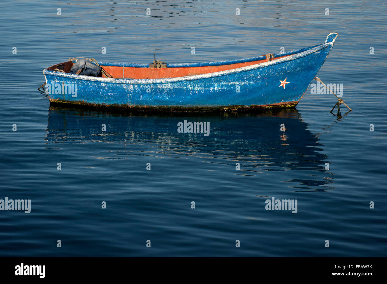 small blue fishing boat moored in blue water Stock Photo