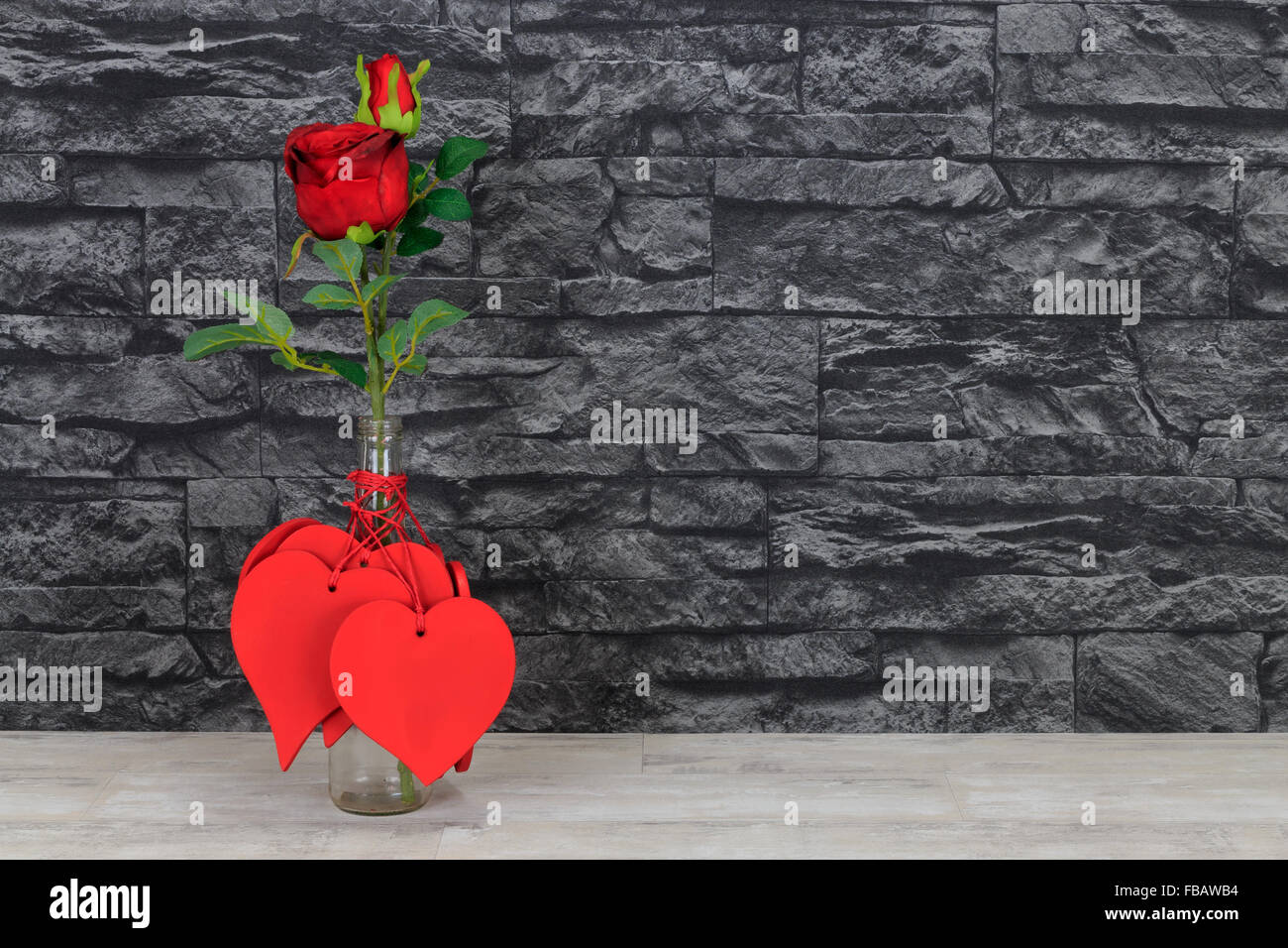Valentine hearts and red rose in glass bottle placed on a shabby wood shelf with black stone wall  background Stock Photo