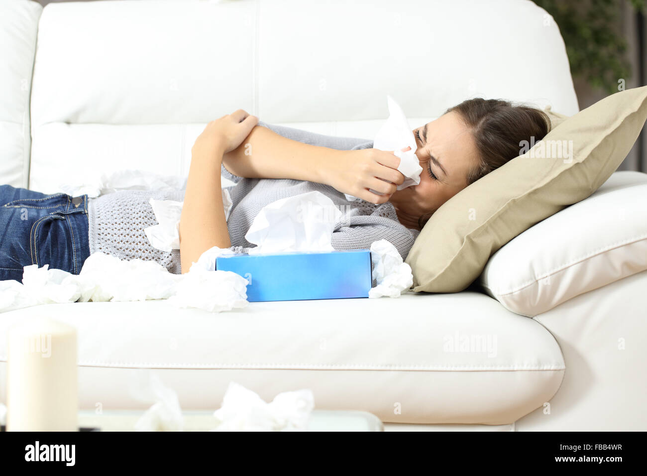 Ill woman sneezing in a tissue lying on a couch at home. Flu concept Stock Photo