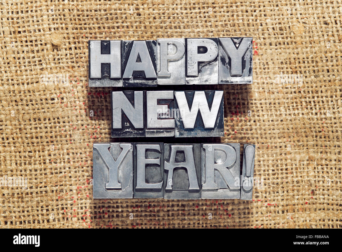 happy new year exclamation made from metallic letterpress type on vintage rough canvas Stock Photo