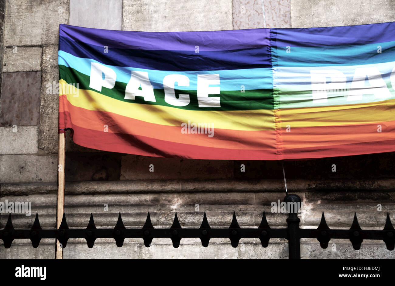 dramatic rainbow peace flag during a demonstration of Italian pacifists in a square behind grates sharp Stock Photo