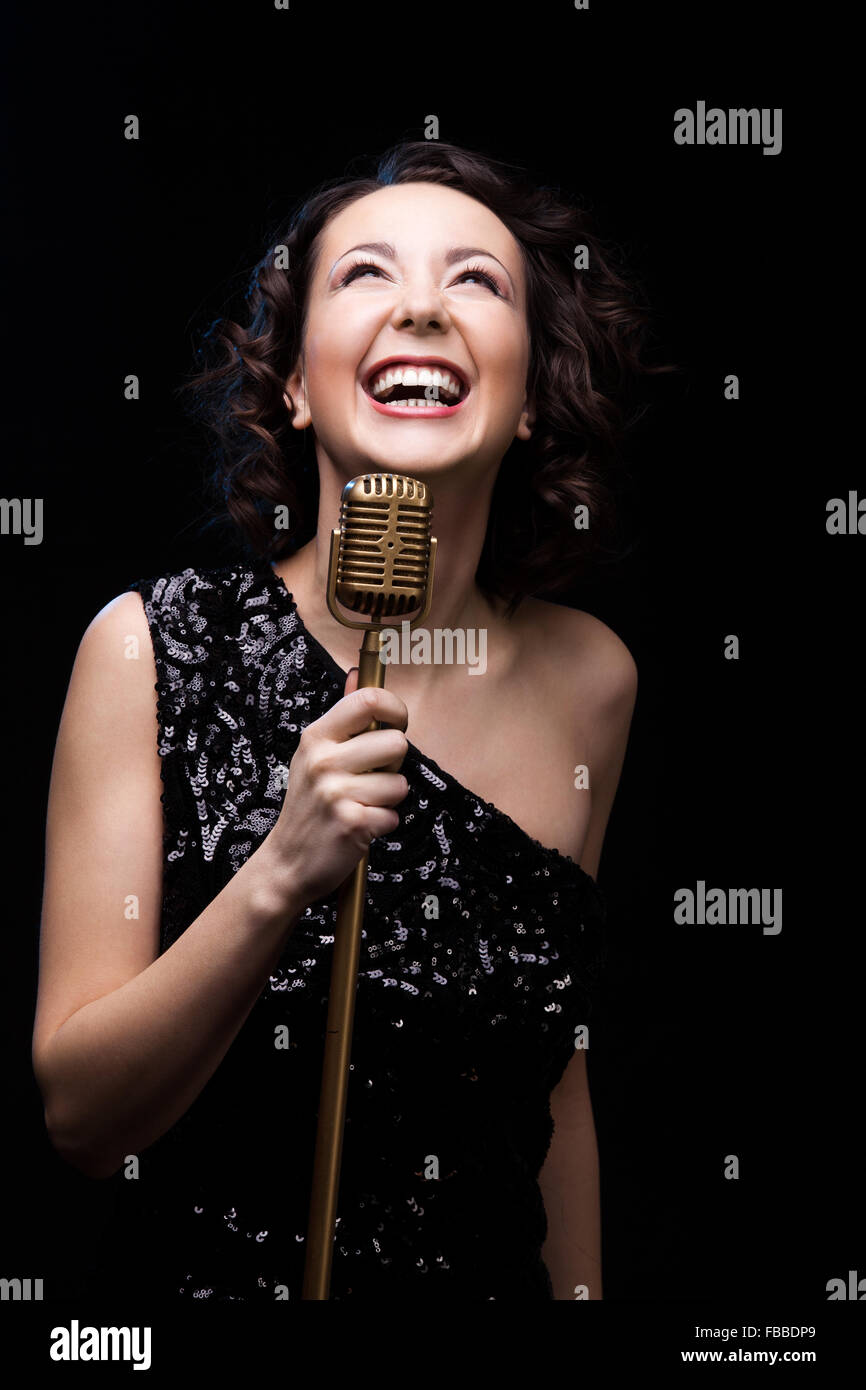 Beautiful young female vocalist in shiny black evening dress happily