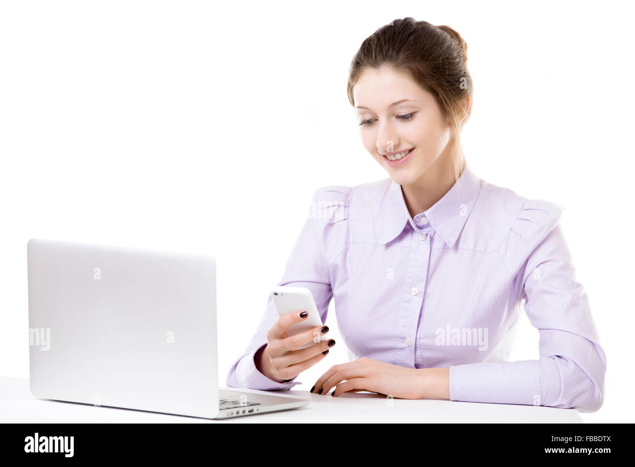 Beautiful office girl in formal wear seating with laptop, typing message on mobile phone, texting, using app on smartphone, rece Stock Photo