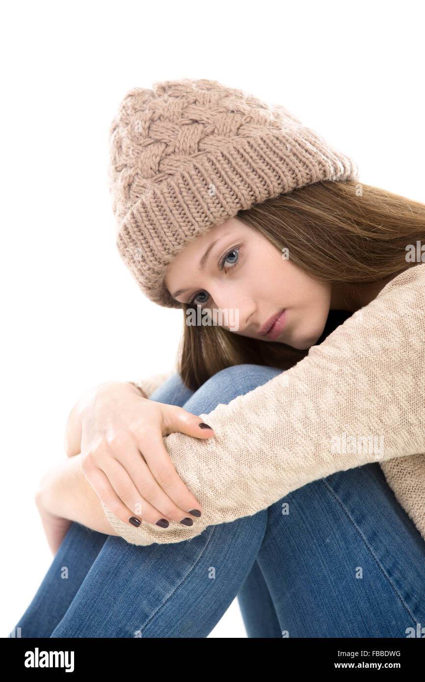 Teens troubles. Unhappy teenage girl sitting clasping her knees, looking down Stock Photo
