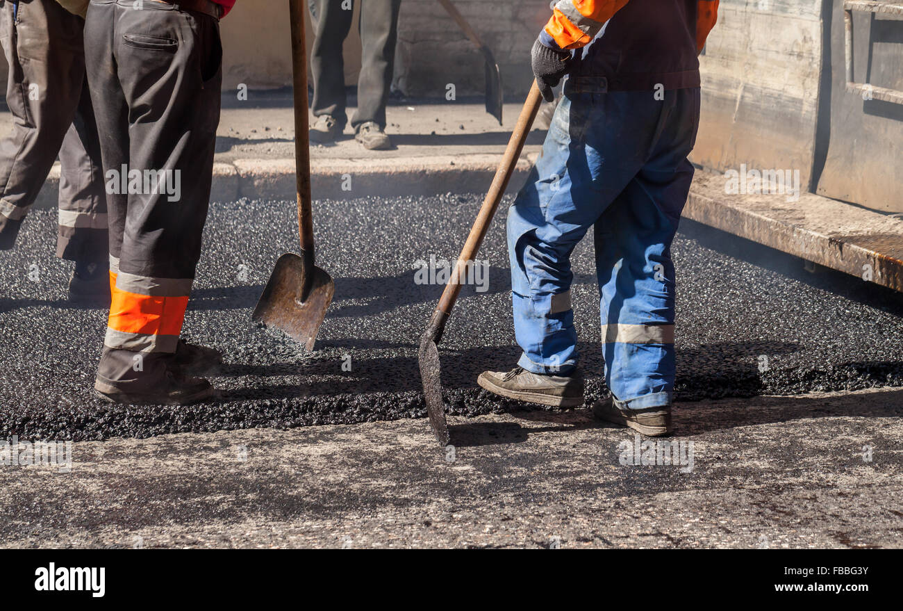 Urban road under construction, asphalting in progress, workers in uniform with shovels Stock Photo