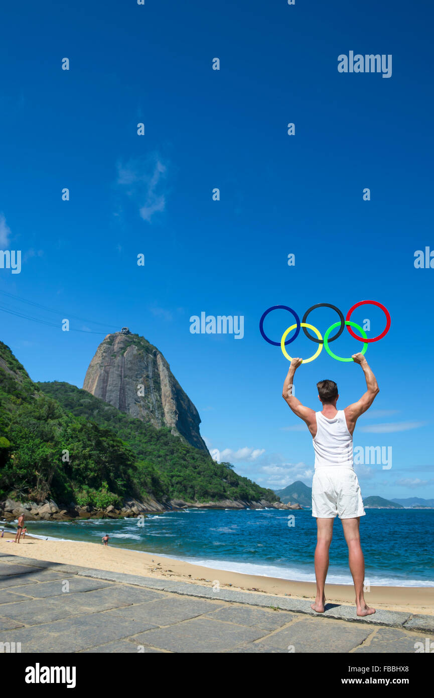 RIO DE JANEIRO, BRAZIL - NOVEMBER 10, 2015: Athlete holds Olympic rings in front of a view of Sugarloaf Mountain at Red Beach. Stock Photo