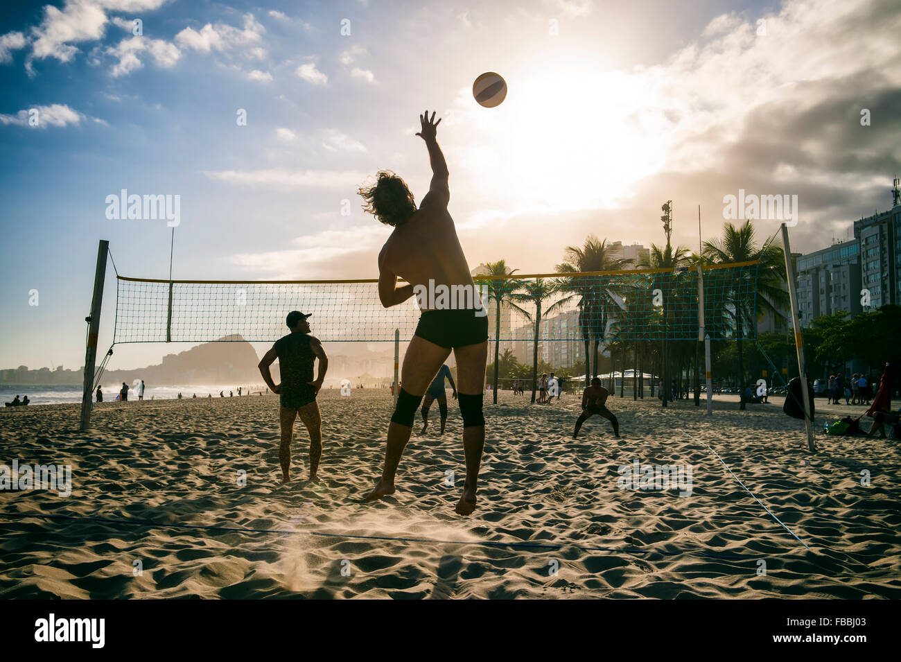 RIO DE JANEIRO, BRAZIL - OCTOBER 30, 2015: A group of young Brazilian men play game of volleyball at sunset on Copacabana Beach. Stock Photo