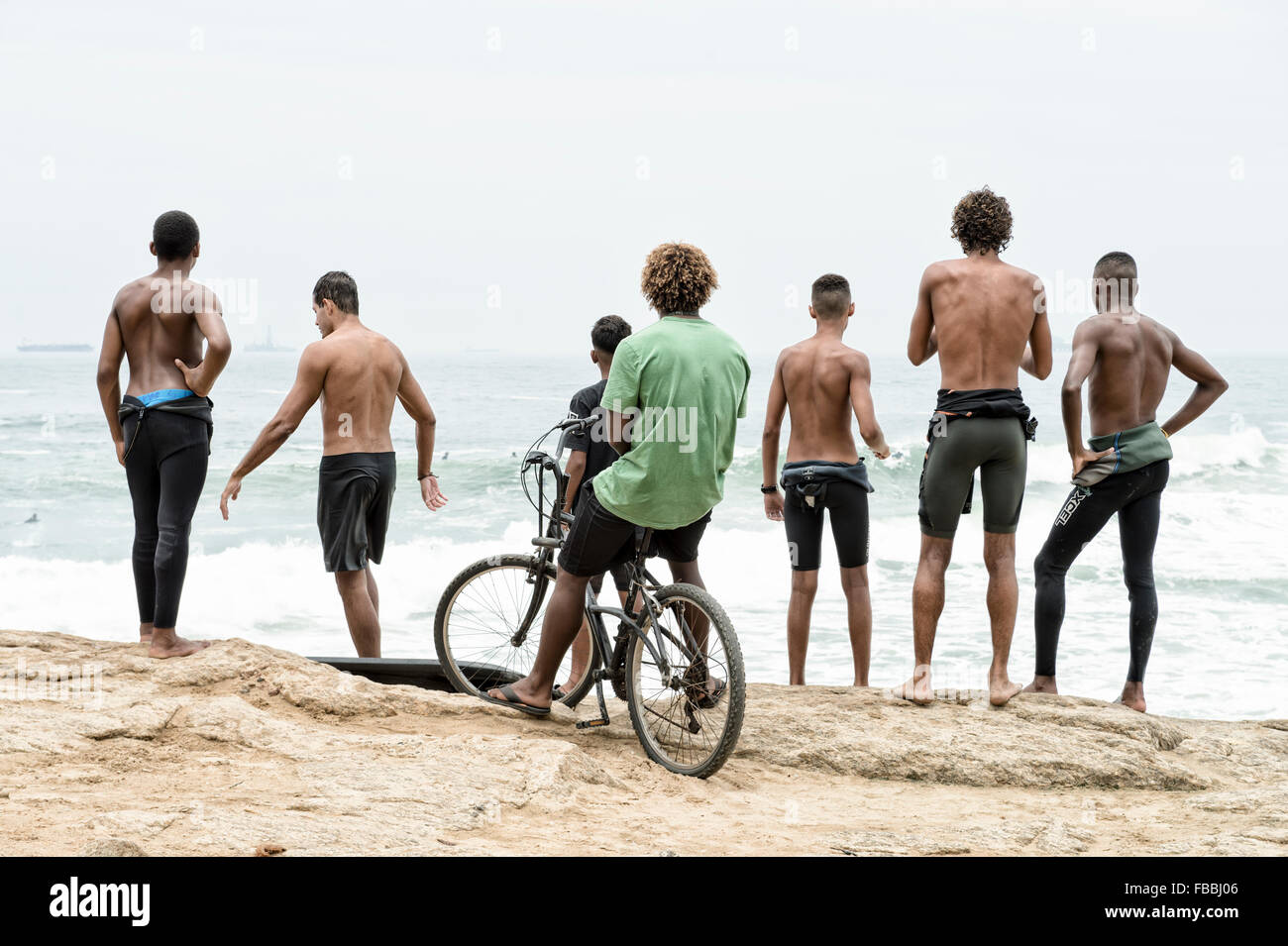 RIO DE JANEIRO, BRAZIL - OCTOBER 22, 2015: Brazilian surfers in wetsuits stand looking at incoming surf waves at Arpoador. Stock Photo