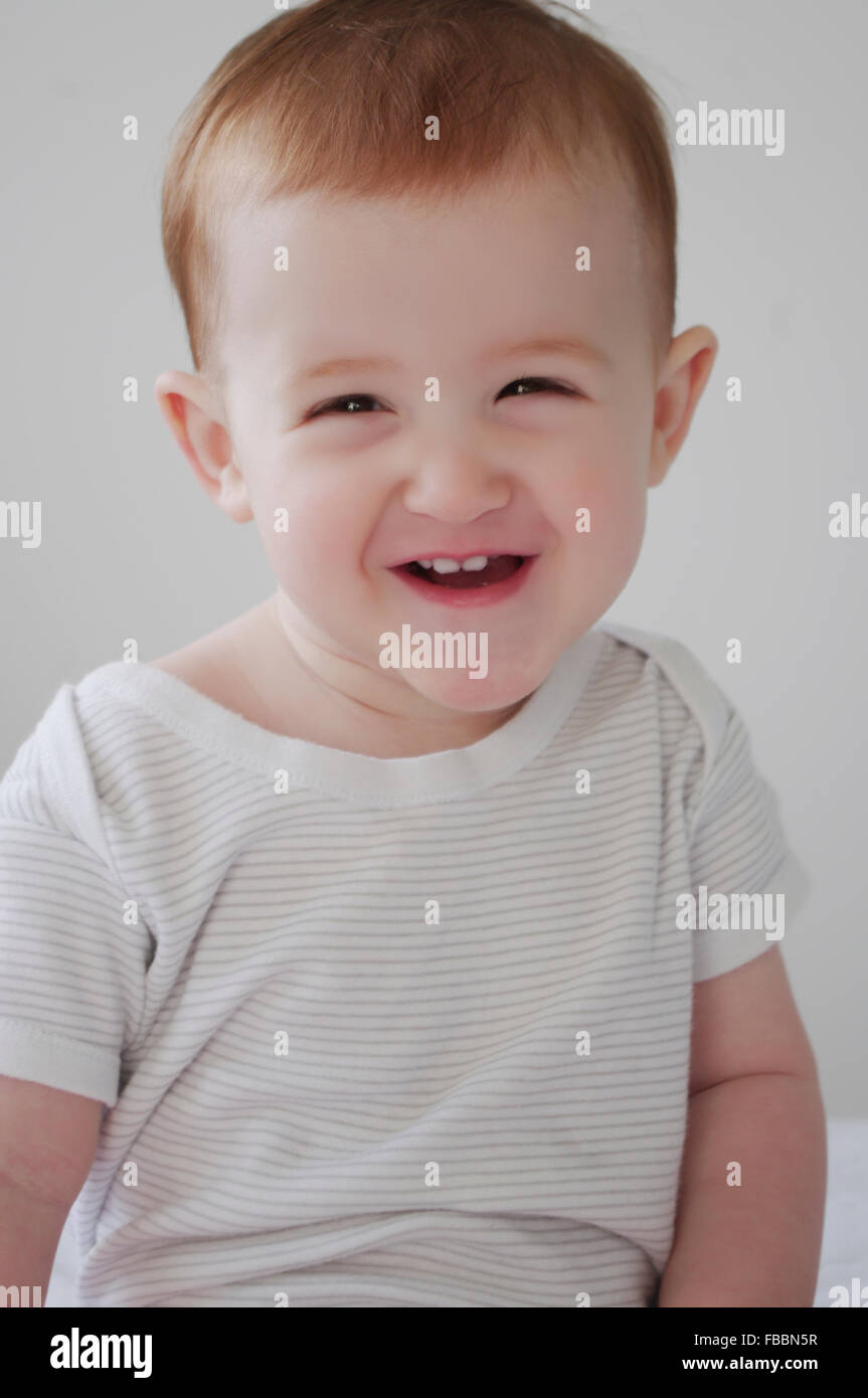 Portrait of a cute red haired Caucasian baby girl wearing a striped white vest Stock Photo