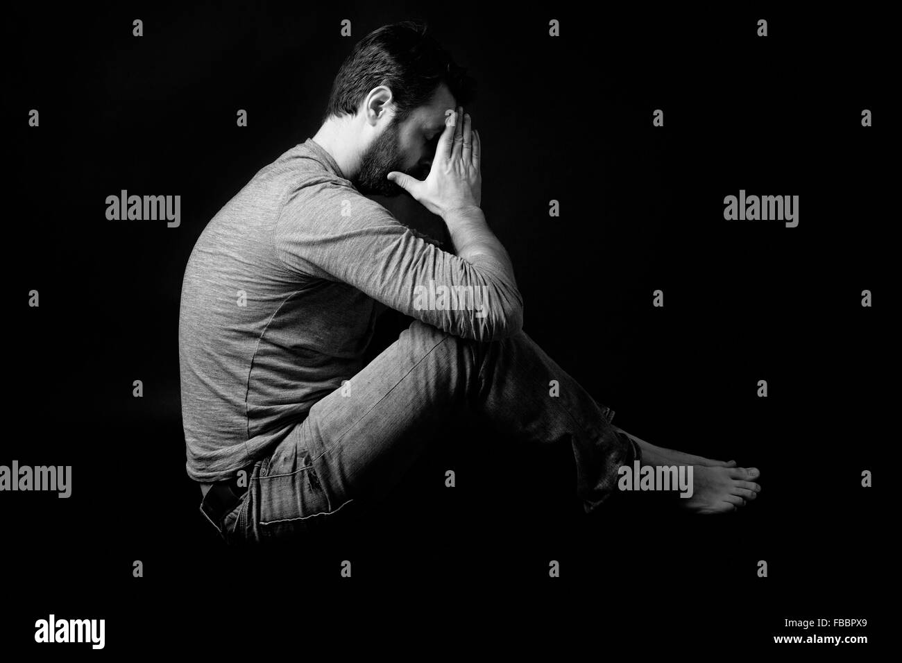 Low Key Portrait Of Man Sitting In Dark And Contemplating Stock Photo low-key-portrait-of-man-sitting-in-dark-and-contemplating-stock-photo