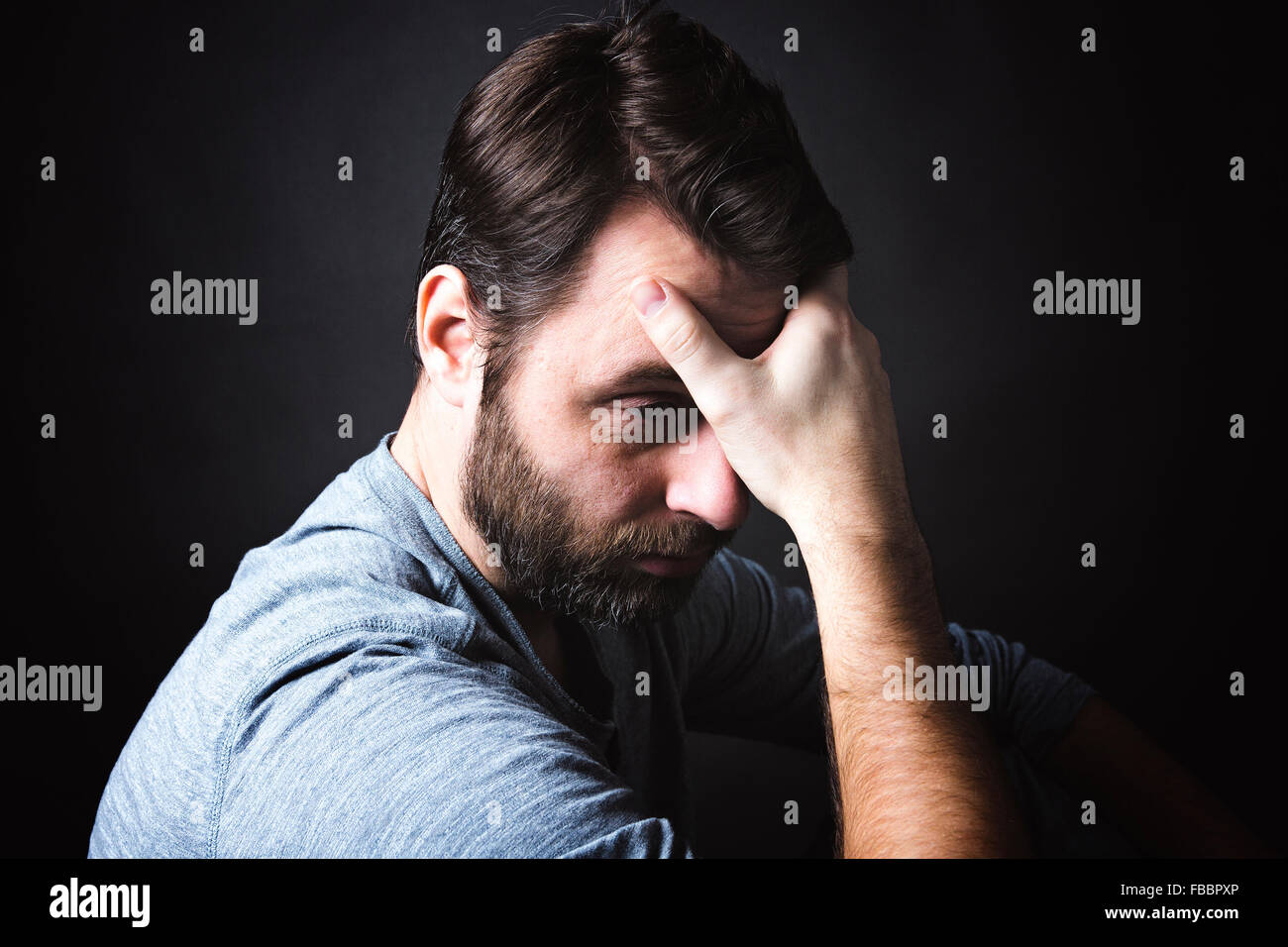 Low Key Portrait Of Man Sitting In Dark And Contemplating Stock Photo low-key-portrait-of-man-sitting-in-dark-and-contemplating-stock-photo