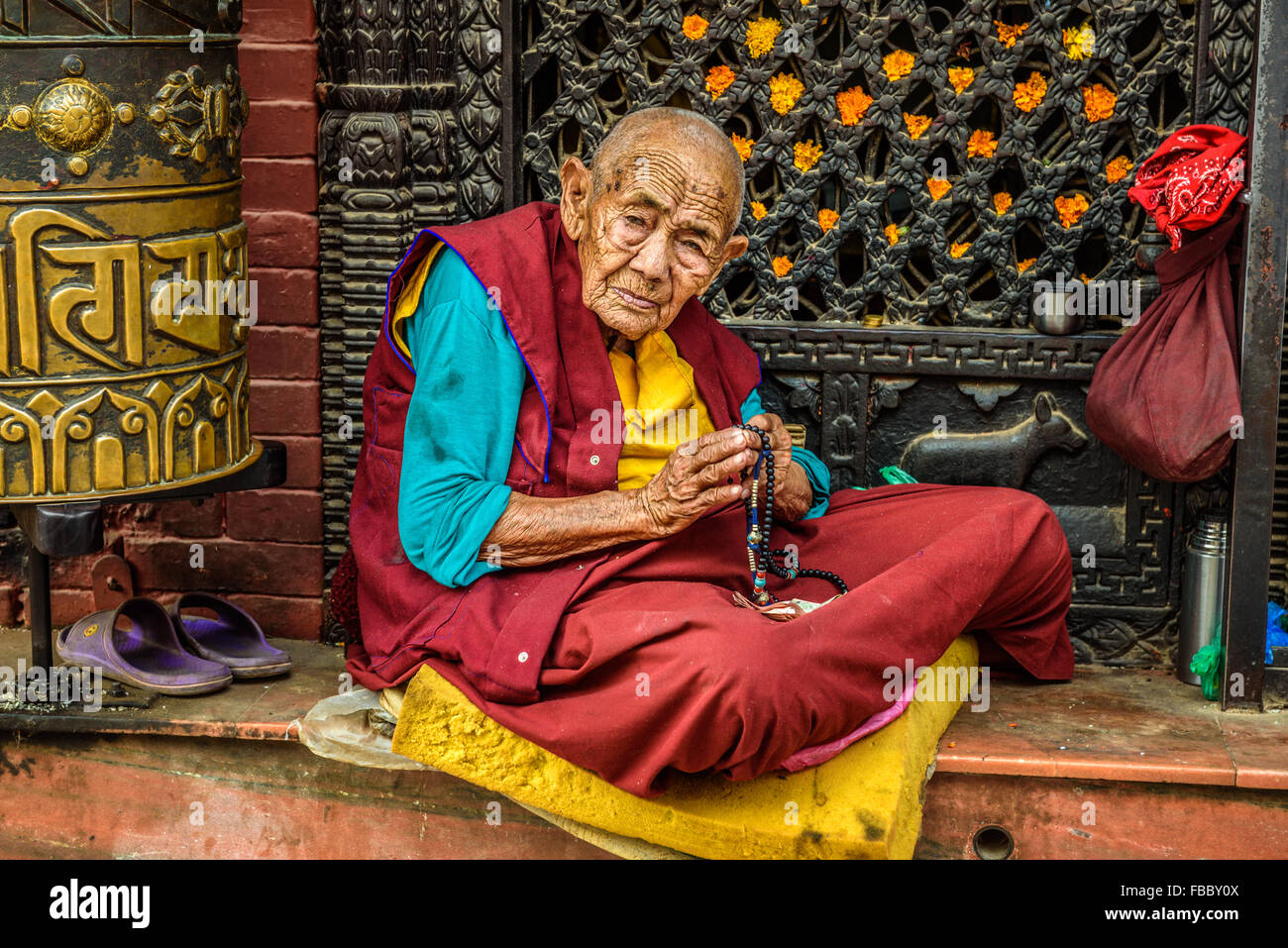 Very old tibetan buddhist nun sits and begs outside a shrine in Kathmandu Stock Photo