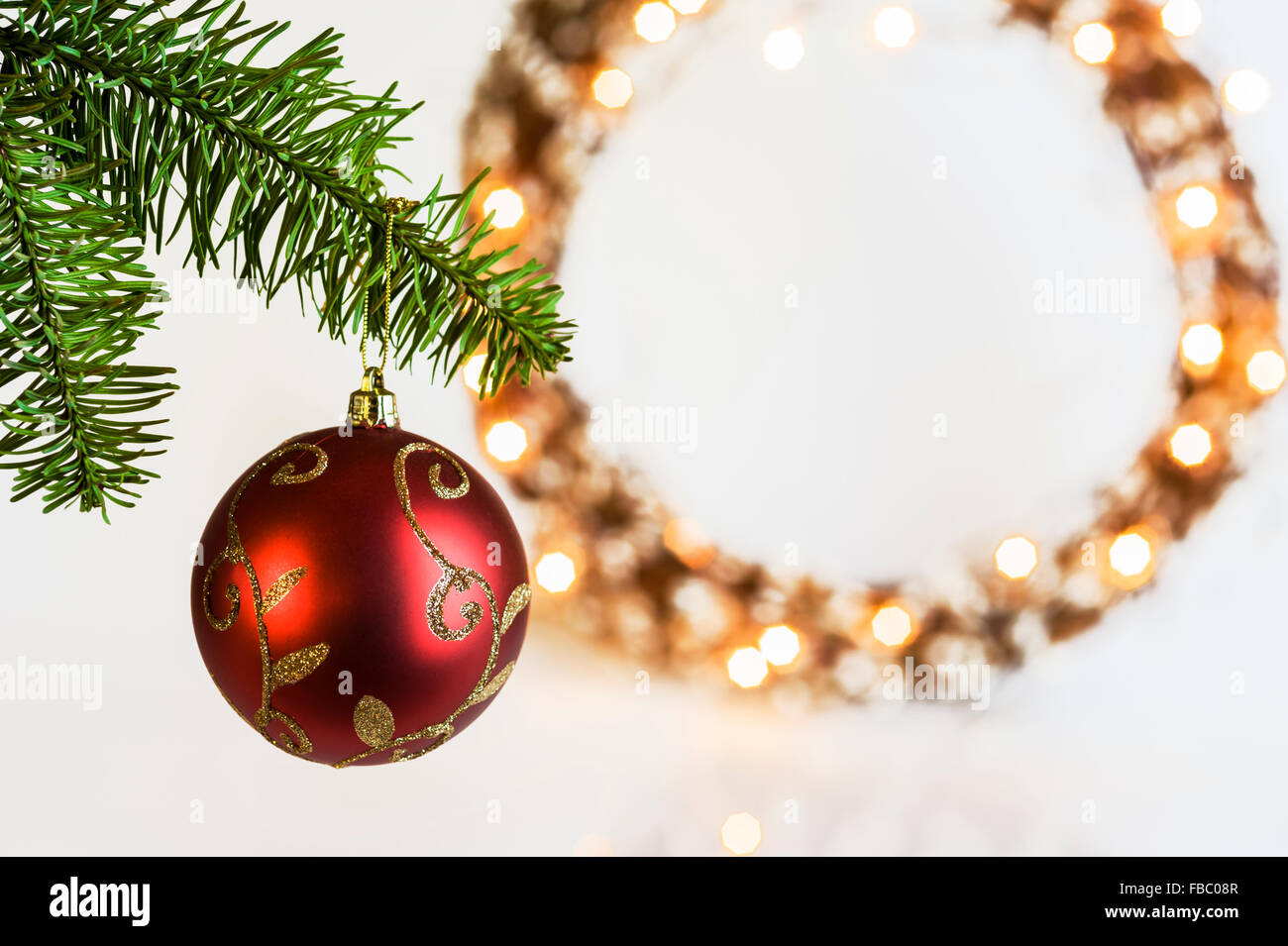 Red Christmas bauble with illuminated wreath behind. Stock Photo