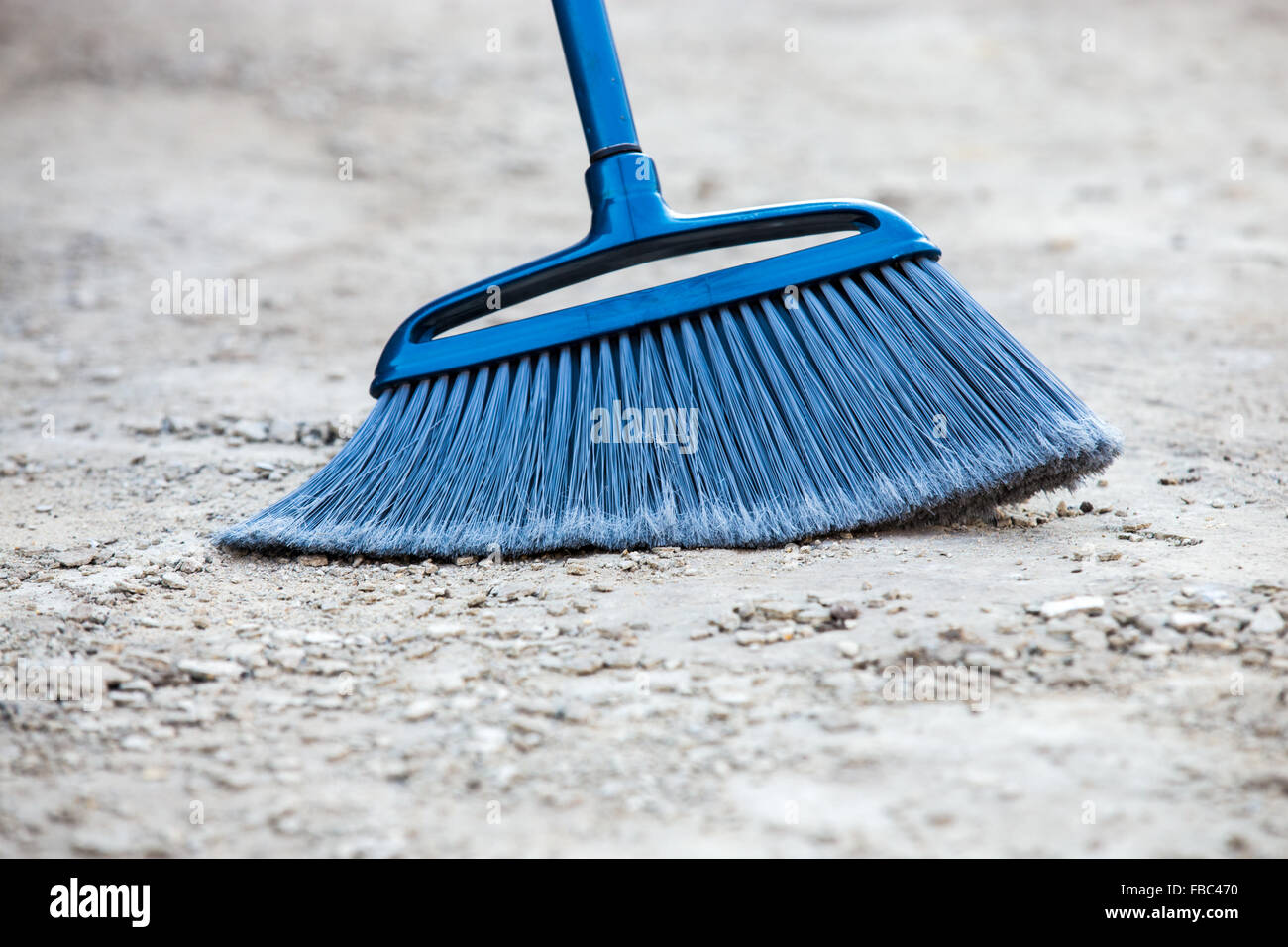 Close up of blue broom brushing grey crumbled concrete sidewalk outdoors, cleaning Stock Photo