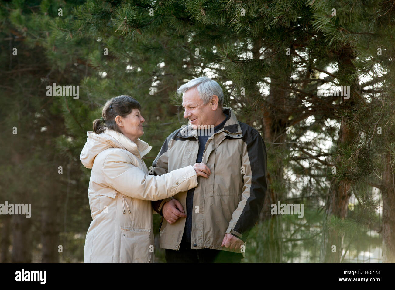 Senior couple enjoying a walk in park, laughing, joking, looking at each other with love, elder lady playfully adjusting her hus Stock Photo