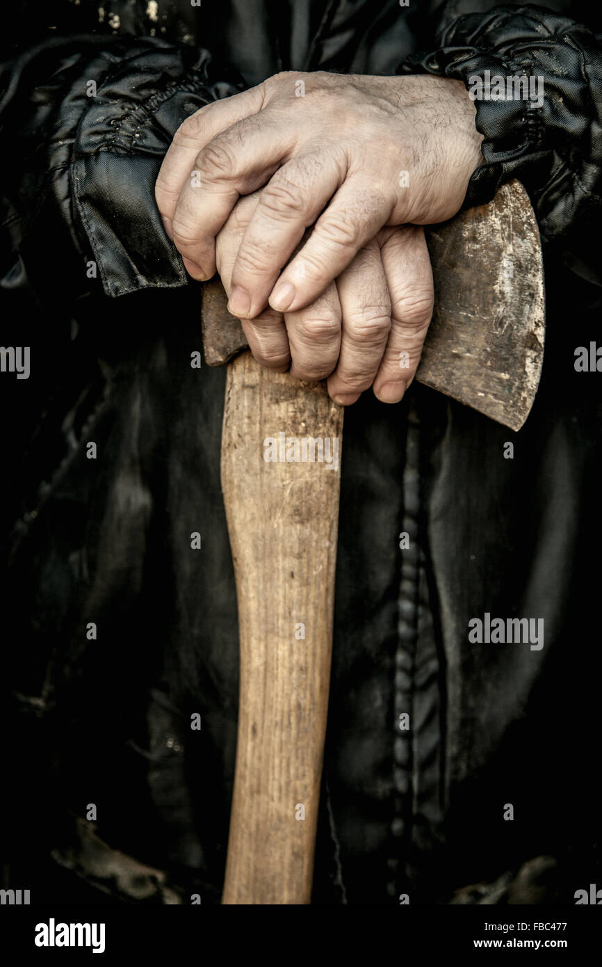 Close-up of scruffy male hands resting on old rusty axe with dirty wooden handle Stock Photo