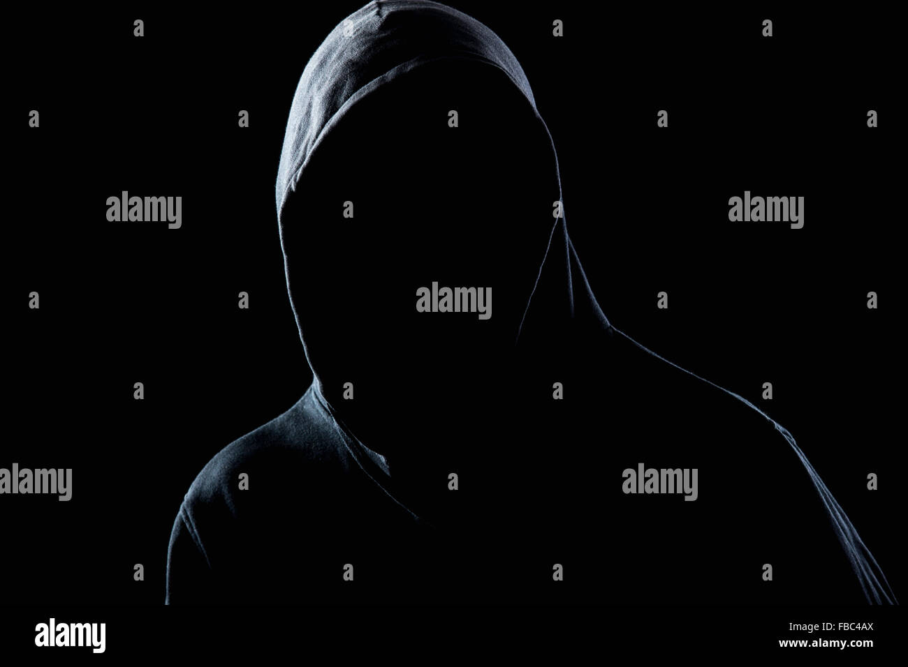 Young man in black hooded sweatshirt invisible in the night darkness, dimly lit, concepts of danger, crime, terror Stock Photo