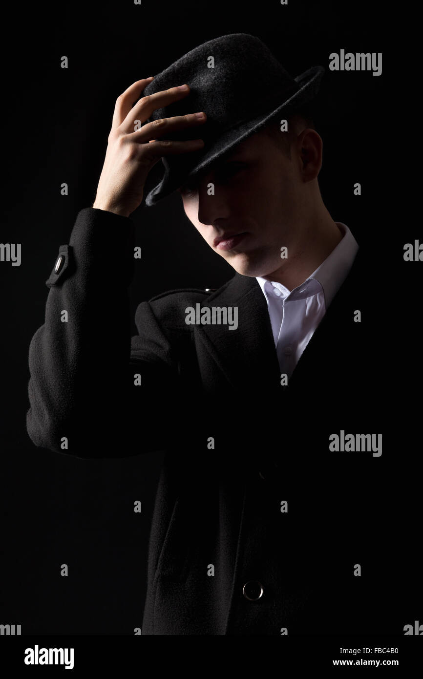 Handsome unrecognizable elegant mafioso man in coat touching his hat as in  greeting, scarcely visible in the darkness Stock Photo - Alamy