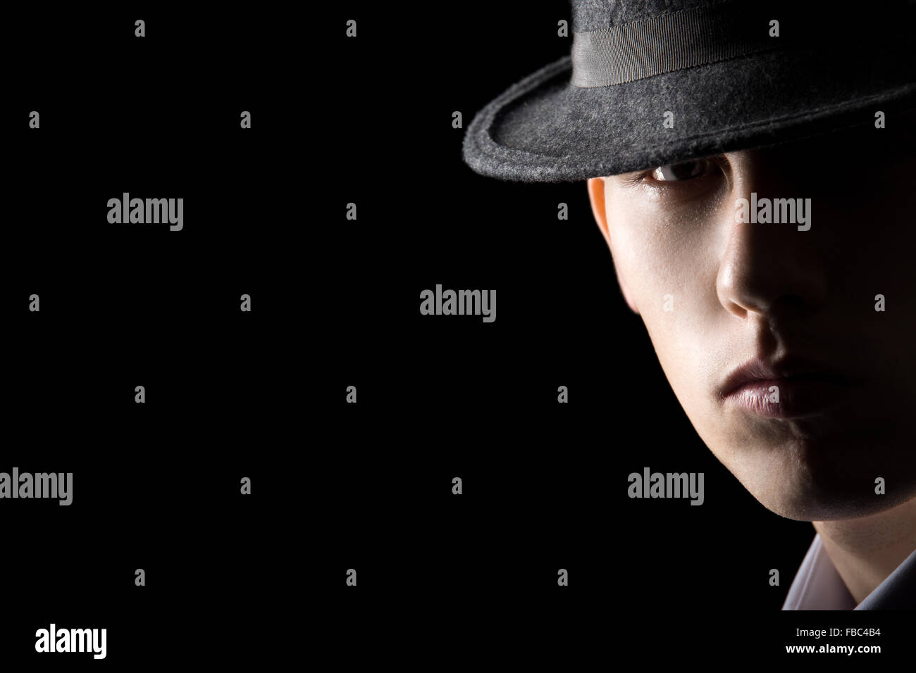 Portrait of young man in hat, his face half lit, brutal, serious, calm, studio shot against black background, low key lighting w Stock Photo