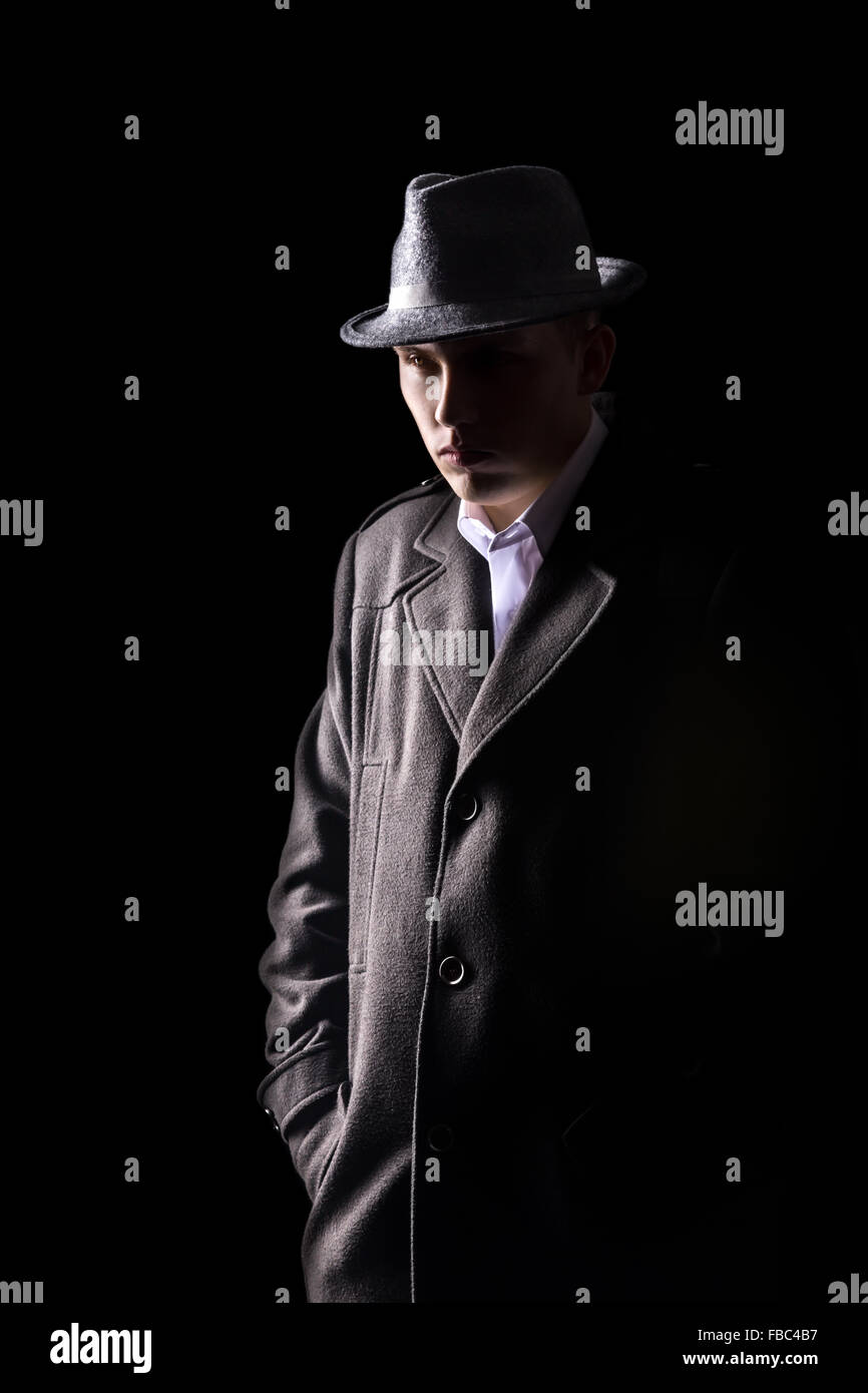 Portrait of mysterious Caucasian man in black hat and coat with tough expression walking in darkness, low key studio shot agains Stock Photo