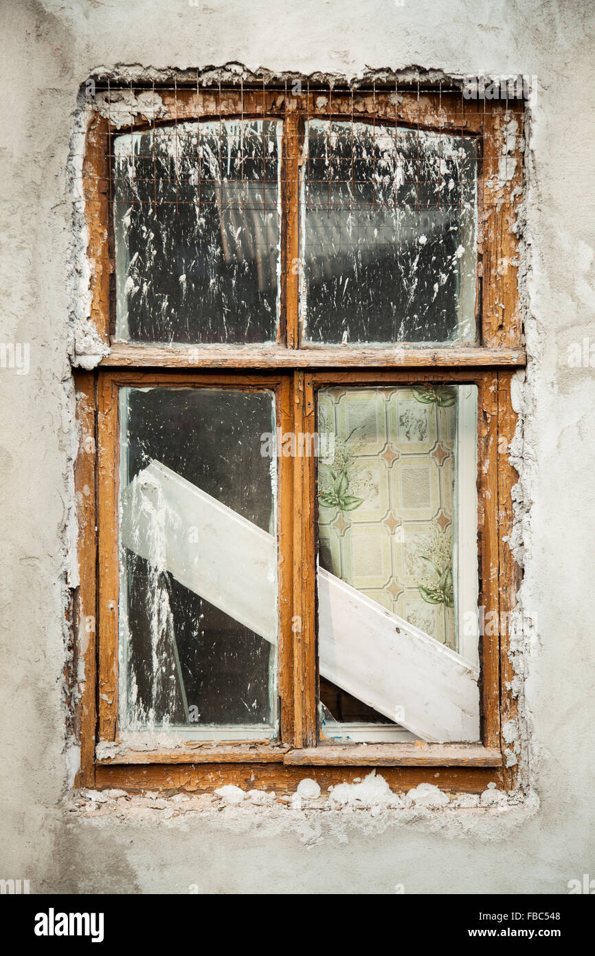 Background of rundown white stucco wall with wooden window covered in