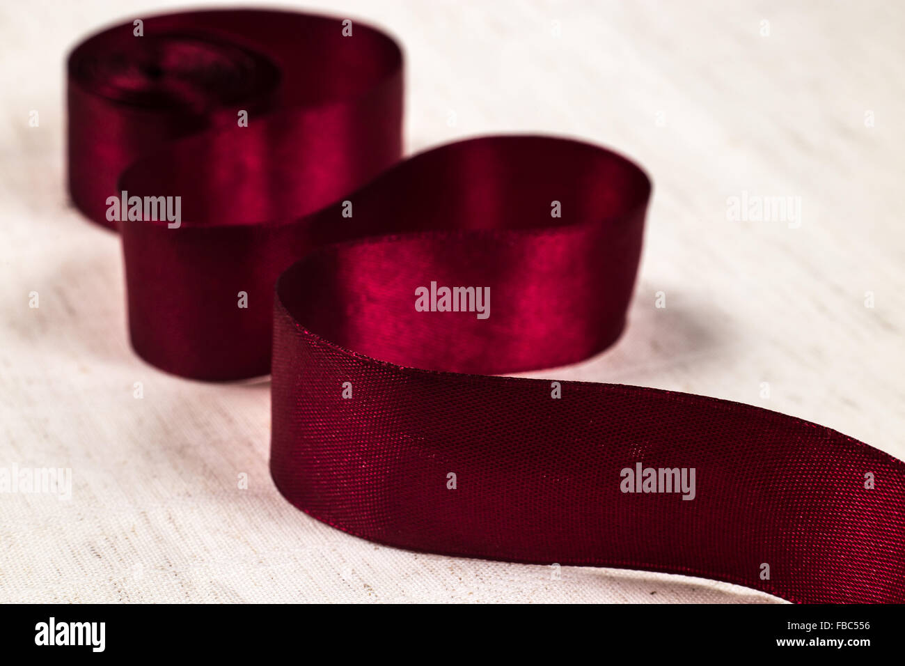 Close-up of deep red ribbon unraveling on white background Stock Photo