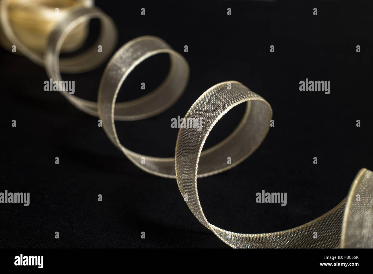 Close-up of white transparent ribbon spiral unwinding in perspective on black background Stock Photo