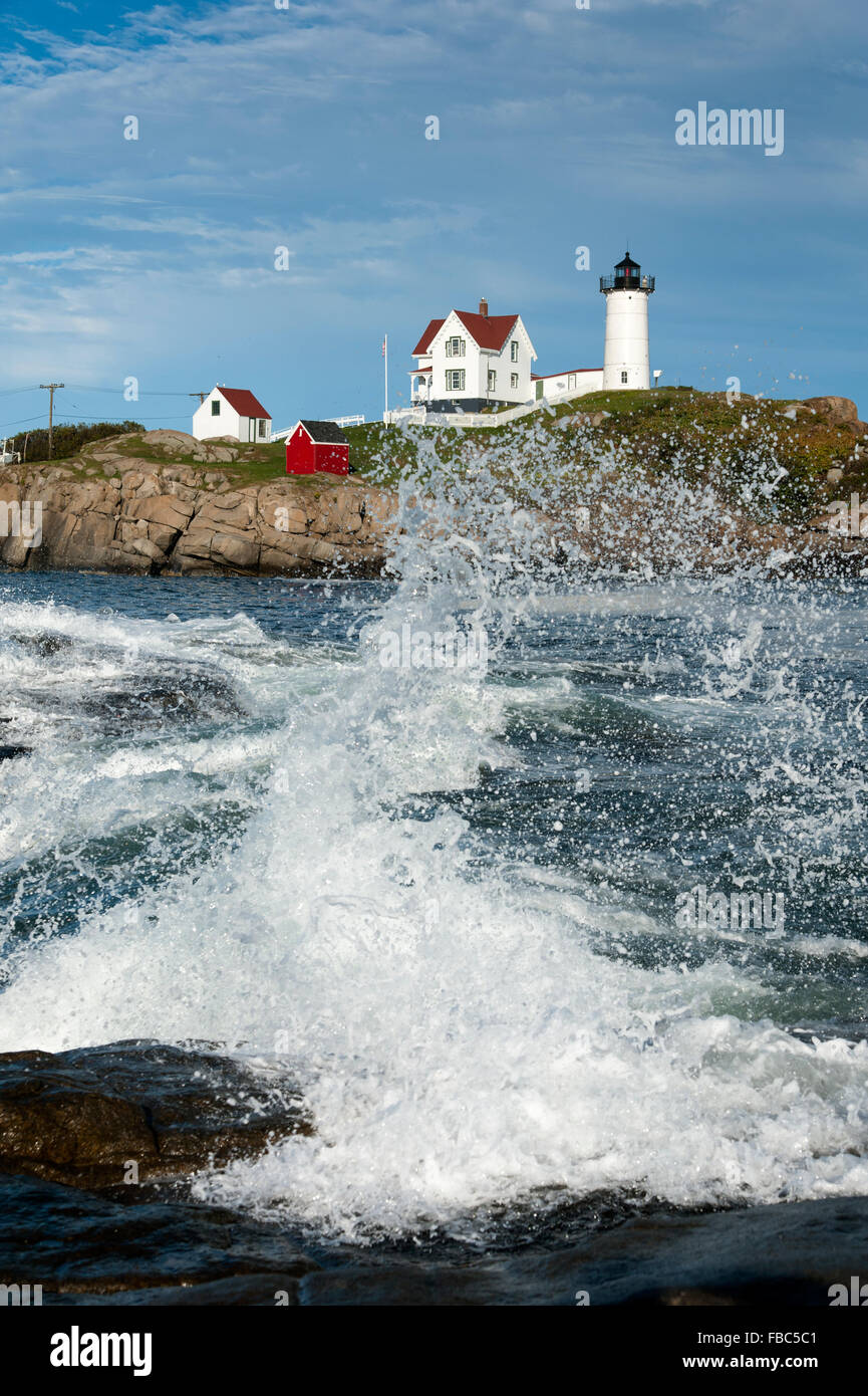 Wave breaks on rocky shore at high tide in front of Nubble (Cape Neddick) lighthouse in Maine. Stock Photo