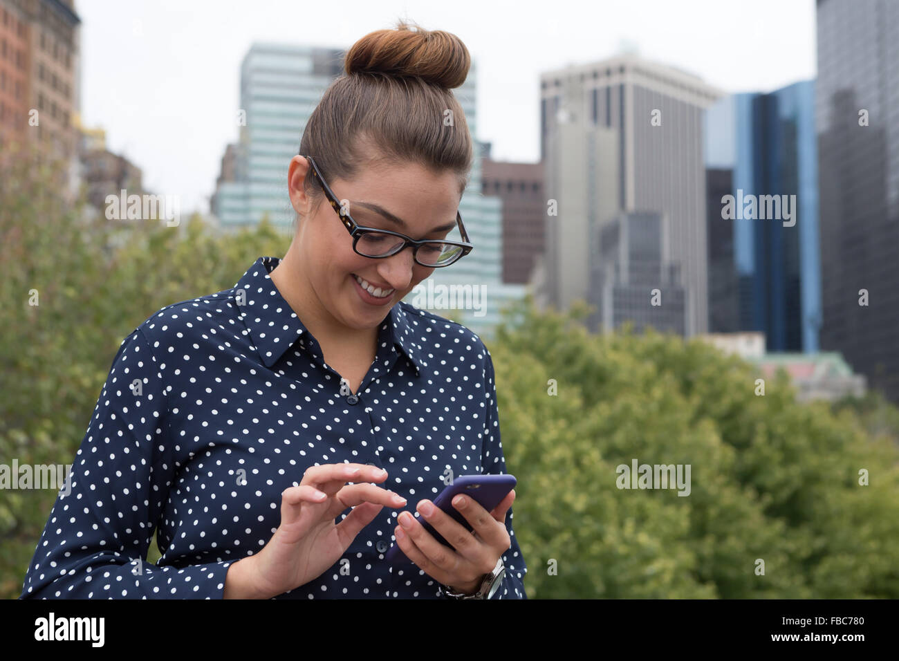 A young professional business woman texting with highrise building in the background. Photographed in New York City, in October Stock Photo