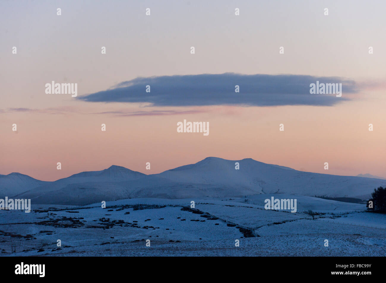 Brecon Beacons, Powys, Wales, UK. 14th January, 2016. A cloud hangs over the snowy peaks of The  Brecon Beacons as the day ends. 5cm of snow fell on high land in Powys last night. Credit:  Graham M. Lawrence/Alamy Live News. Stock Photo