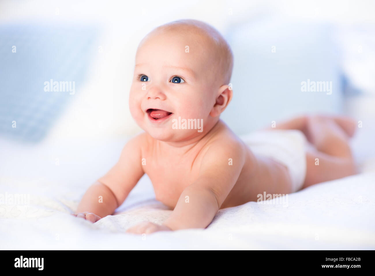 Baby boy wearing diaper in white sunny bedroom. Newborn child relaxing in bed. Nursery for children. Textile and bedding for kid Stock Photo
