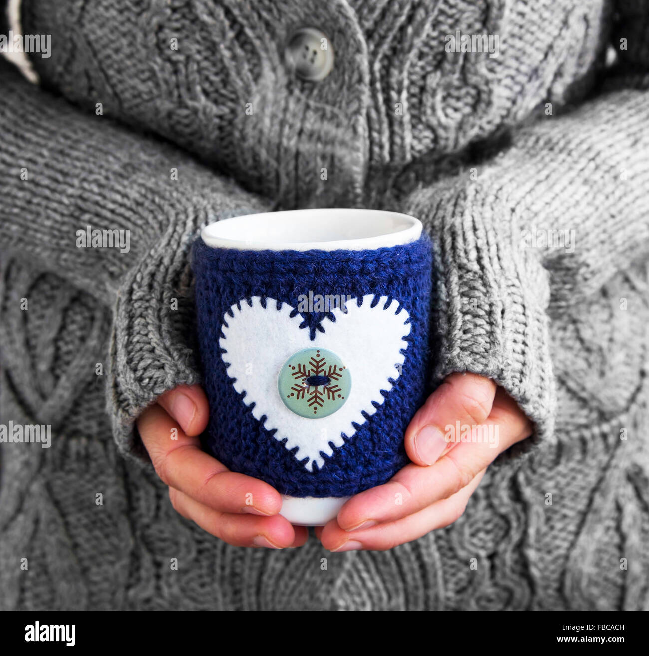 Female Holding Coffee Mug with Knitted Mug Cloth and Heart Shape in the Winter Time Stock Photo