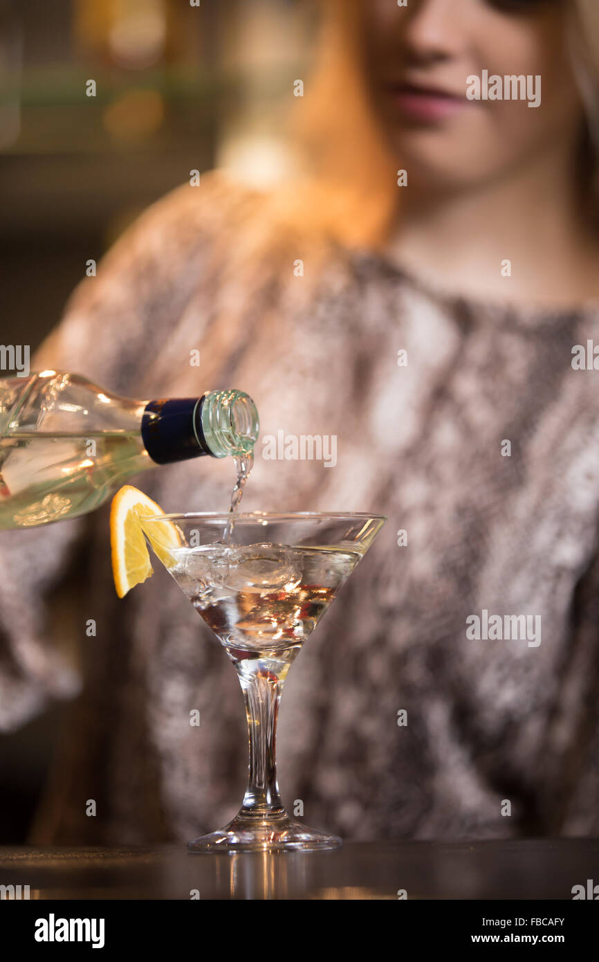 Blond female bartender preparing alcohol drink at bar counter, holding
