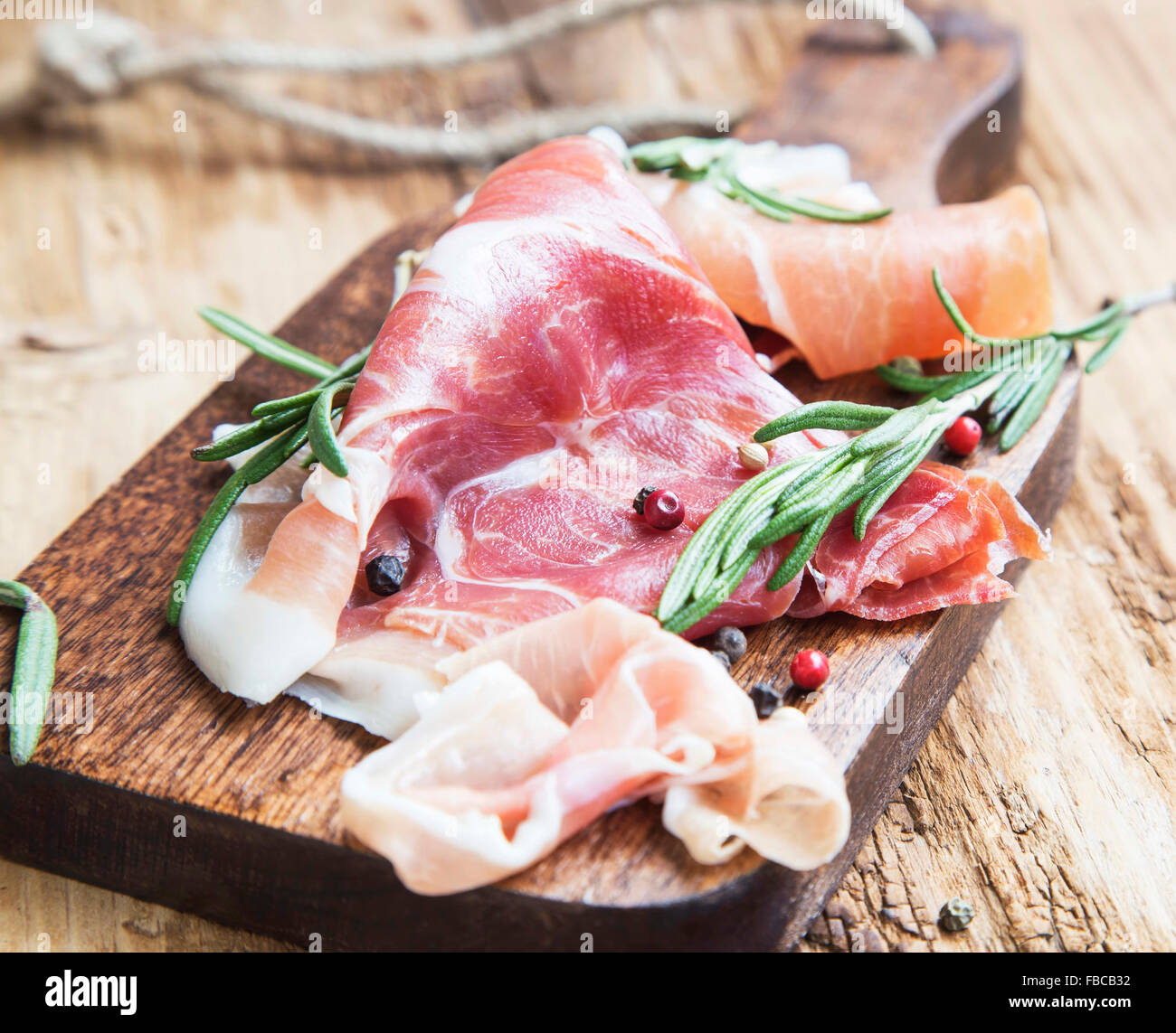 Prosciutto Serrano Ham with Rosemary and Pepper Spice on a Wooden Cutting Board Stock Photo