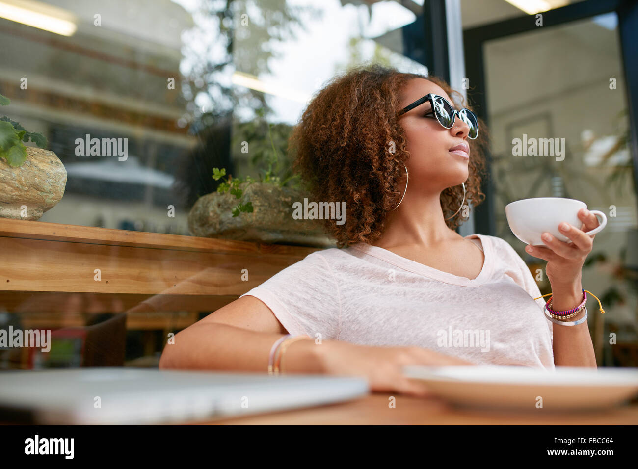 Portrait of attractive young african girl having a cup of coffee at cafe. Stylish young girl drinking coffee at sidewalk cafe. Stock Photo