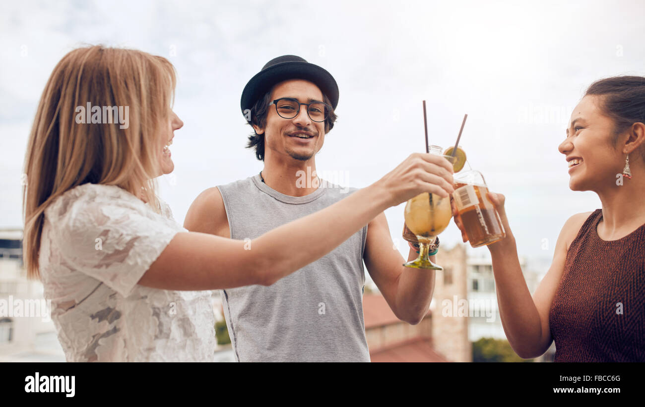 Young men and women hanging out together at rooftop party, toasting drinks. Group of multiracial friends having fun at party. Stock Photo