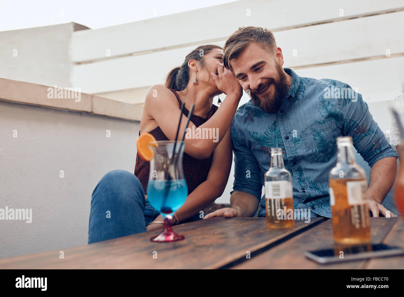 Two young people sitting together gossiping. Woman whispering something in man's ears during a party. Stock Photo