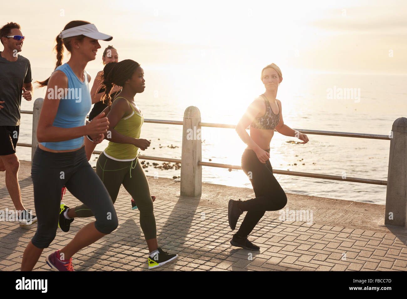 Young people running along seaside at sunset. Closeup image of group of runners working out on a road by the sea. Stock Photo
