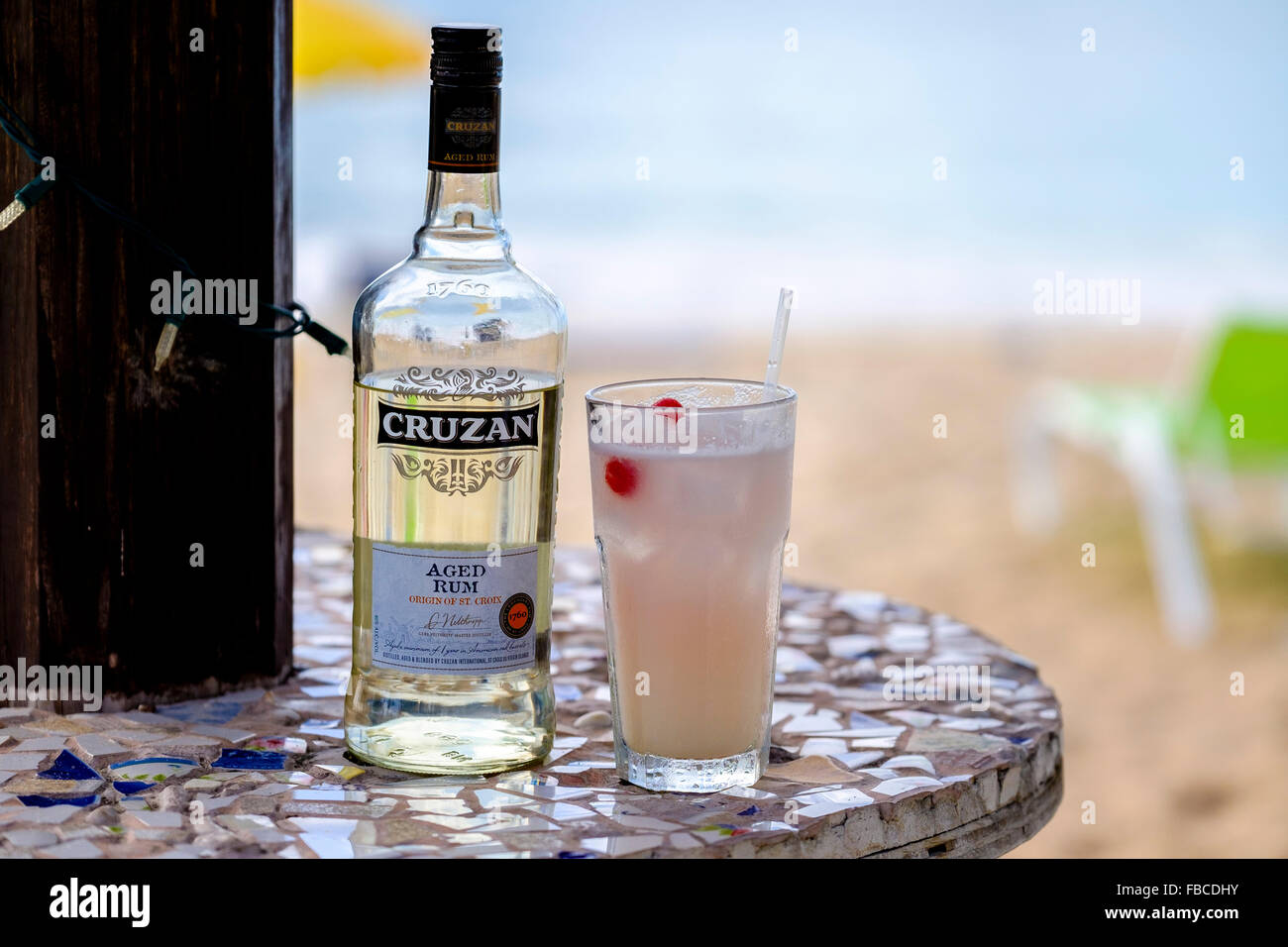A bottle of Cruzan aged rum and a rum cocktail in a glass sitting on a beach table, St. Croix, U.S. Virgin Islands. Stock Photo