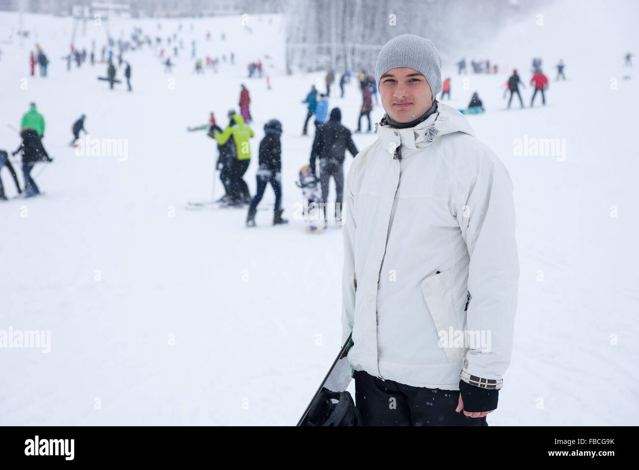 Handsome young man with a snowboard posing on a run at a resort with ...