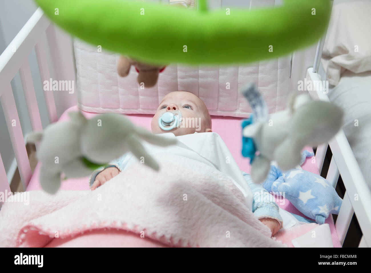 Awake four month baby boy lying in white cot with mobile. Overhead view